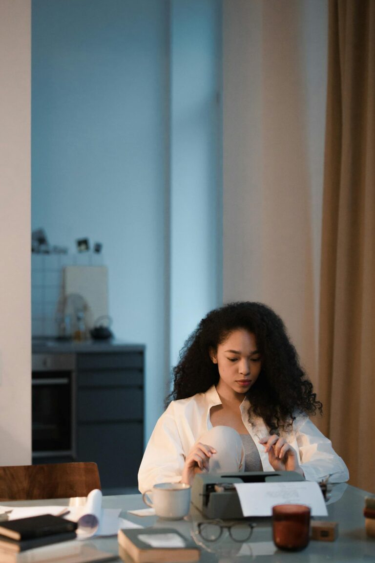 Focused woman with curly hair typing on a typewriter in a dimly lit, cozy room.